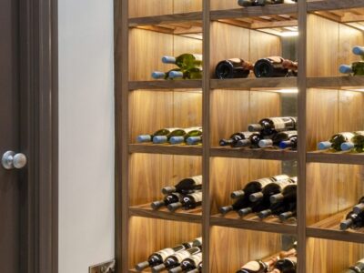 Custom walnut wine rack with integrated lighting and antique mirrored back panels, showcasing wine storage in a hallway.